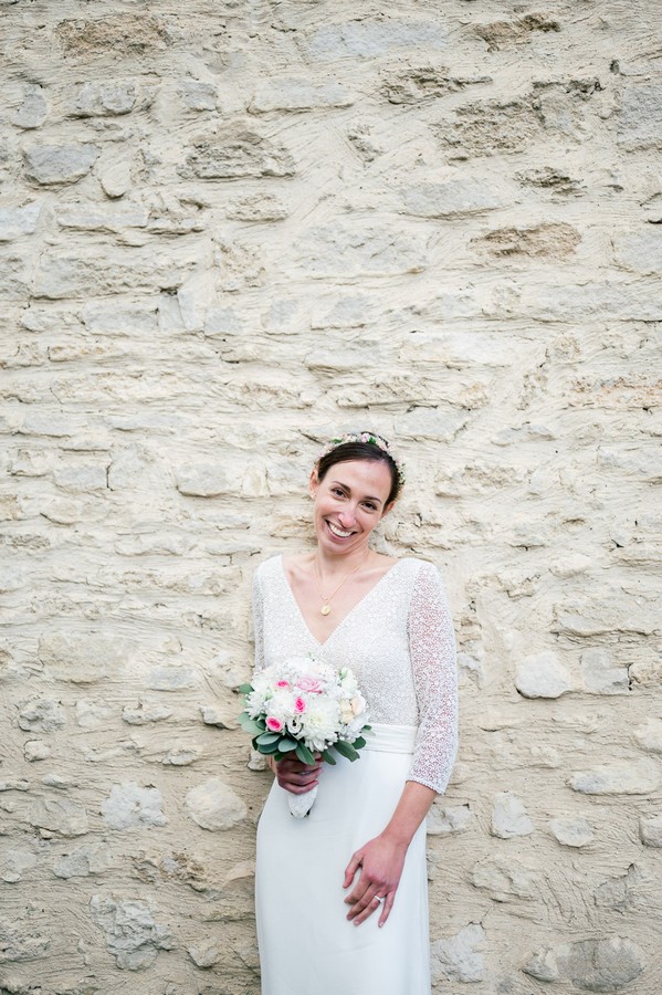 Bride stands with bouquet against rough stone wall
