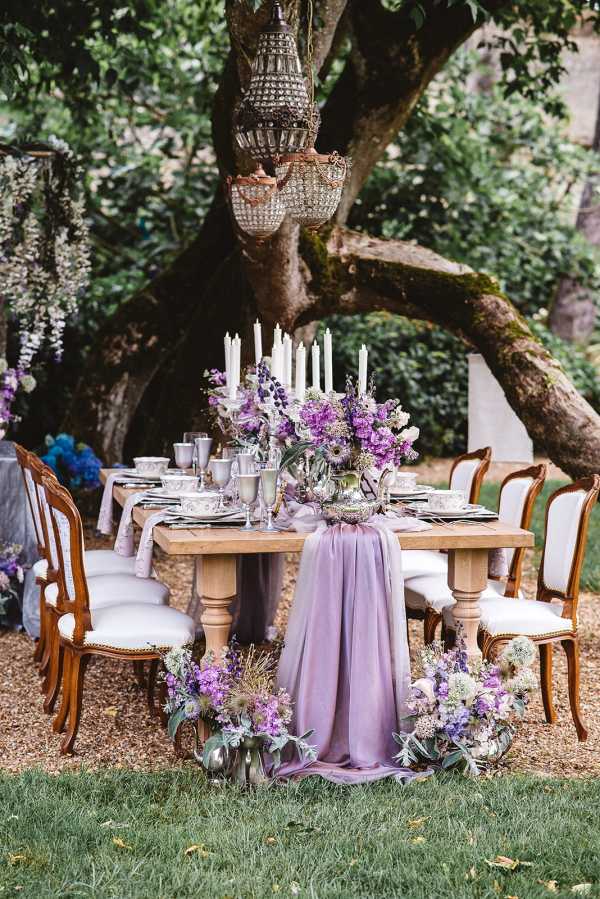 outdoor wedding table setting in purple under tree with crystal chandeliers hanging from its branches