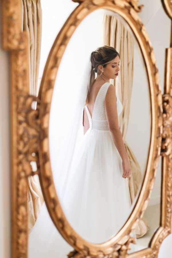 Bride has back turned in reflection through gold gilded mirror