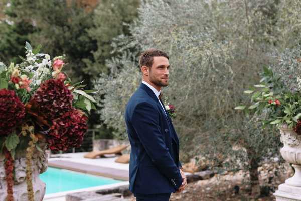 Groom at outdoor altar awaits his bride and looks down the aisle