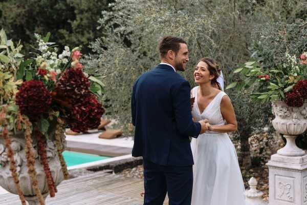 bride and groom smile at each other after their vows are complete surrounded by burgundy floral arrangements