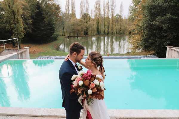 bride and groom lean in for a kiss in front of aqua outdoor pool