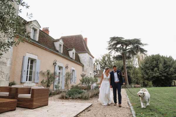 bride and groom walk with dog on lead through the garden outside Chateau Lacanaud in Dordogne France