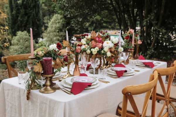 abundant outdoor wedding table decorated with burgundy and pink floral arrangements and tableware