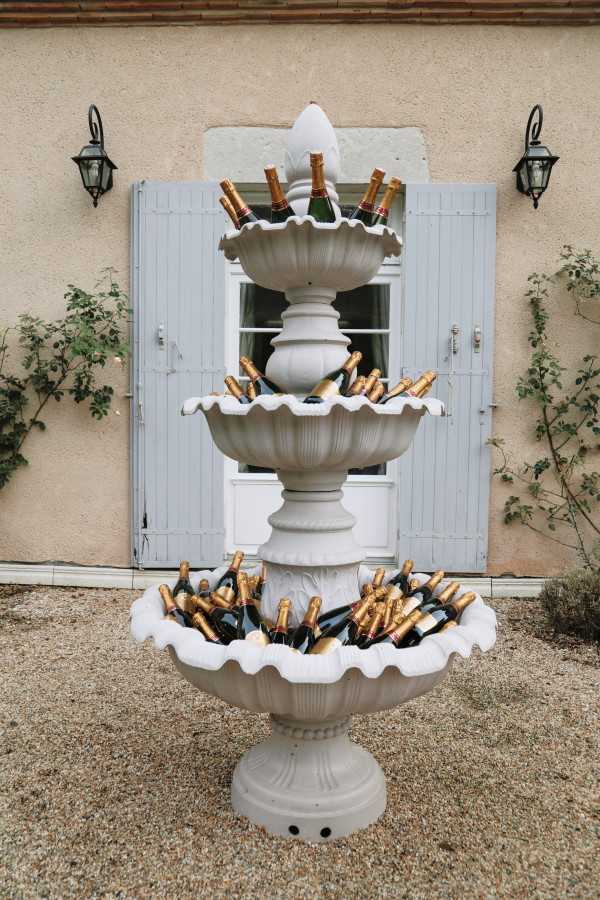 champagne bottles fill a 3 tier outdoor stone water fountain for wedding guests