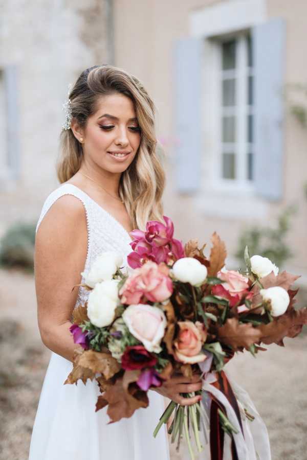 bride smiles and looks down at bouquet of burgundy and pink flowers