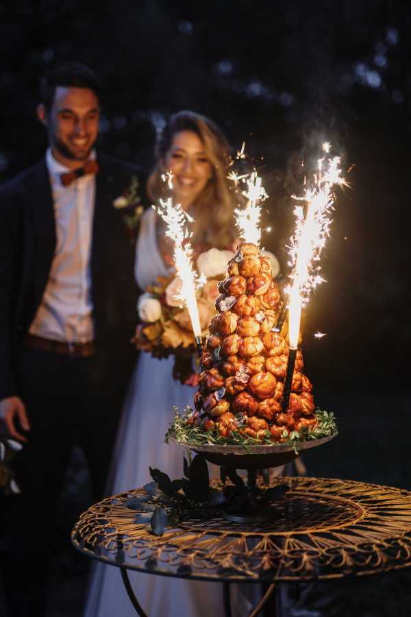 bride and groom smile as sparklers ignite on their croquembouche in the dark