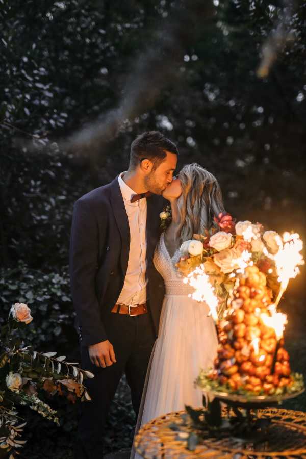 bride and groom kiss in the sparkler light as they cut their croquembouche