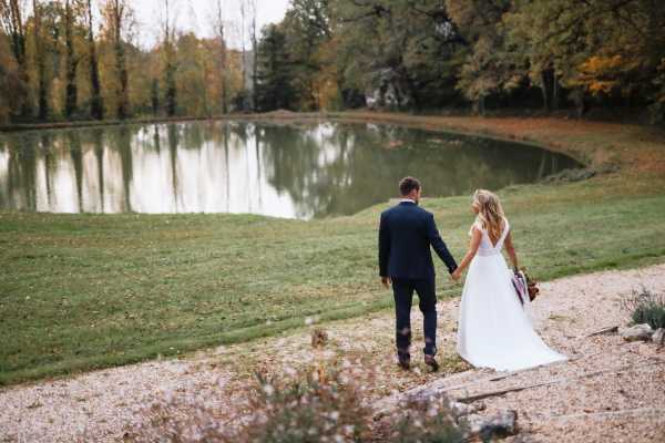 bride and groom hold hands as they cross the grass toward the lake at chateau lacanaud in dordogne, France