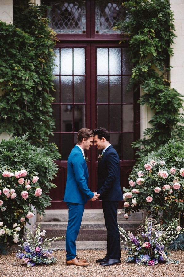 gay couple wearing blue and black suits are just married and touching forehead to forehead