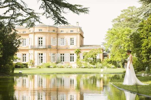 bride outside french chateau looking into still lake water surrounded by green trees