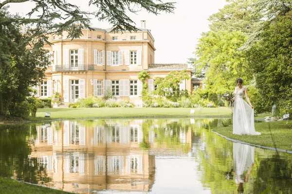 bride by lake outside french chateau which is reflected on water