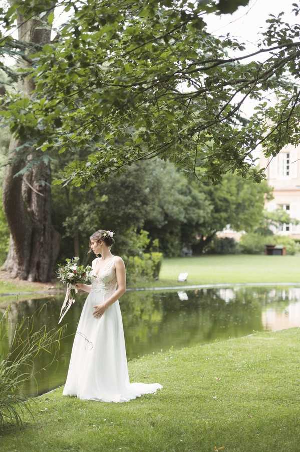 bride in white lace dress in front of lake outside Chateau de Roquefoulet