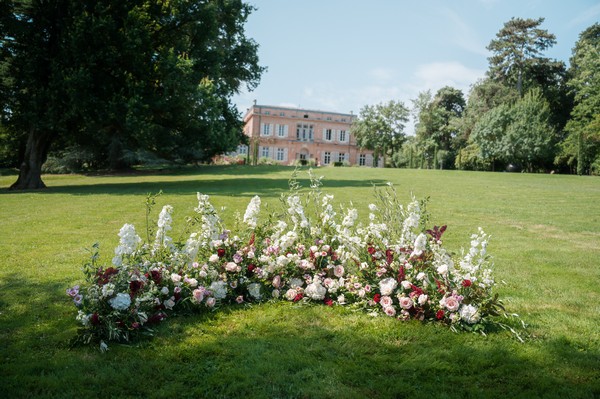 view of french chateau up hill behind floral archway on green lawn