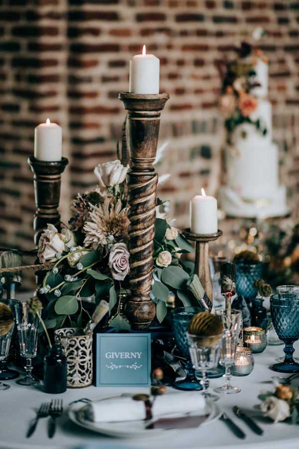 tall golden candle holders with green and brown foliage adorning wedding table