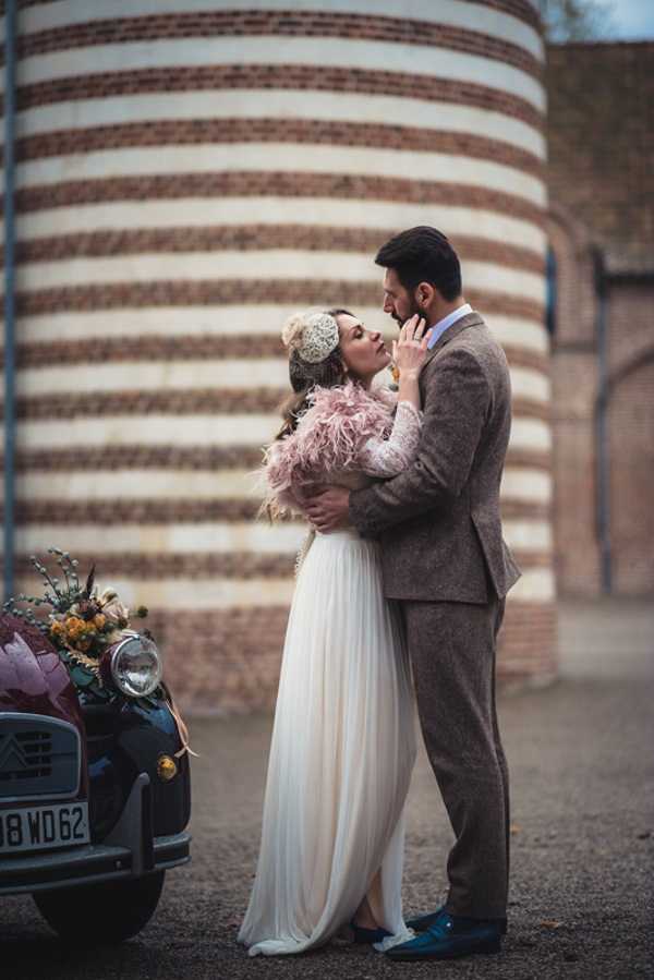 bride and groom kiss in 1920s inspired wedding outfits next to 2 tone bridal car