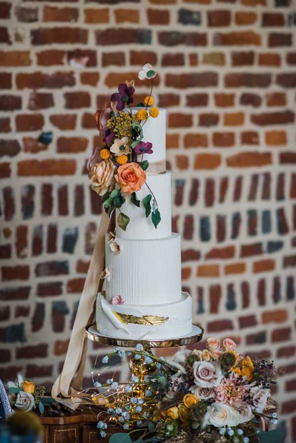 4 Tier rustic white wedding cake with orange flowers cascading down one side