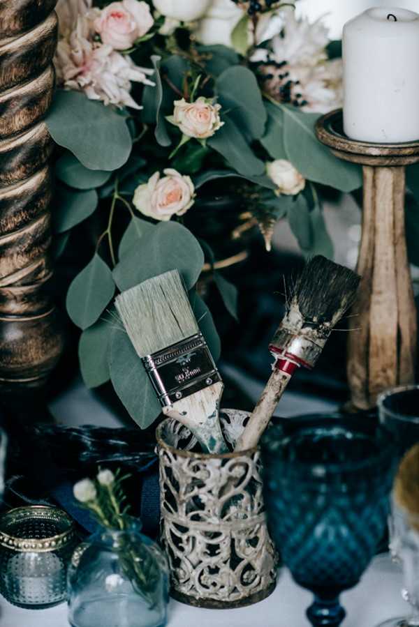 Rustic wedding decoration of green foliage and a cup of used wooden paint brushes