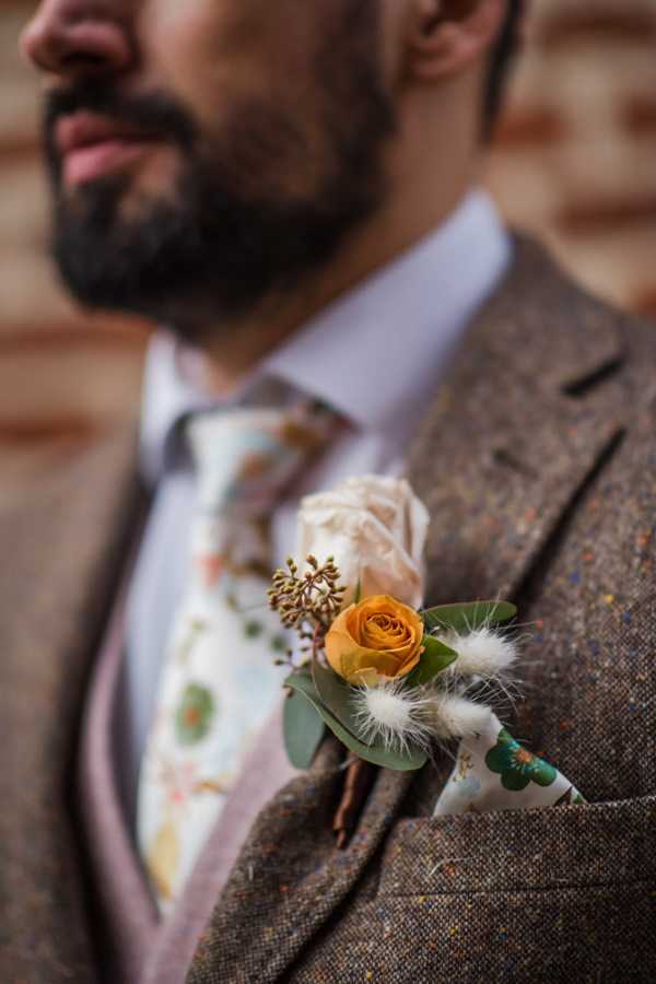 grooms buttonhole of orange an green foliage and berries on a brown tweed suit jacket