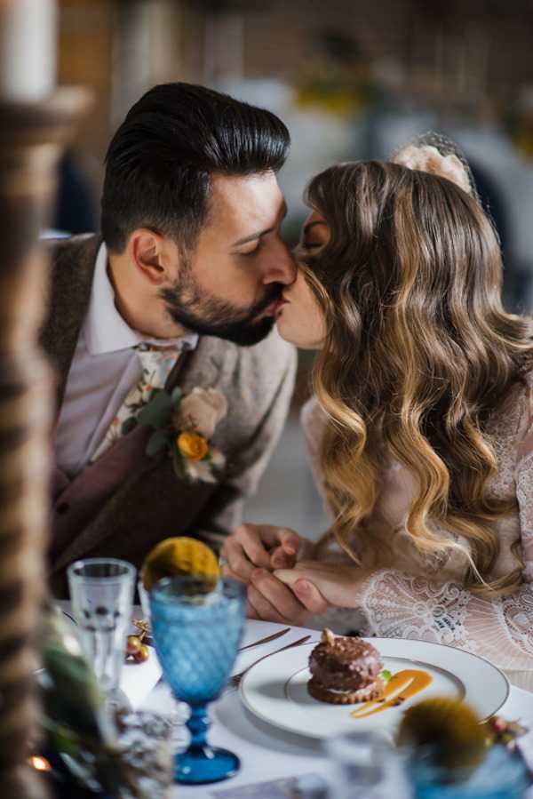 bride and groom kiss at wedding table