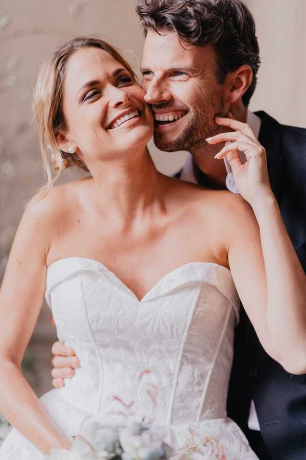 Bride and groom laugh at the camera and the bride touches her grooms face