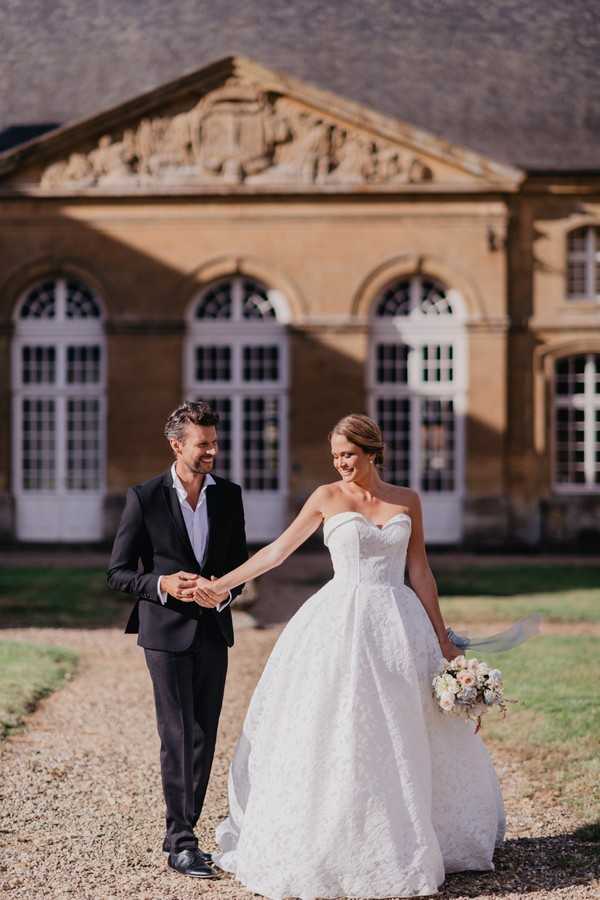 Bride and groom hold hands in the sun outside Chateau Cons La Grandville