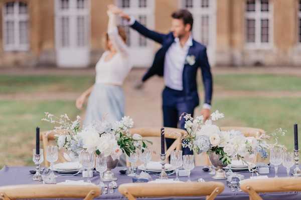 Bride and groom dance in the background behind blue themed wedding table with pastel flowers