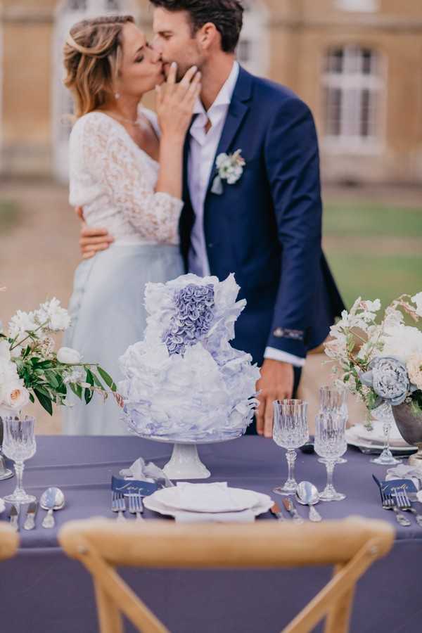 Bride and groom kiss behind blue themed wedding table with blue ruffled wedding cake