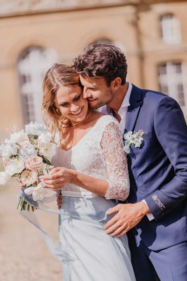 Bride and groom stand back to chest and kiss in the sunshine