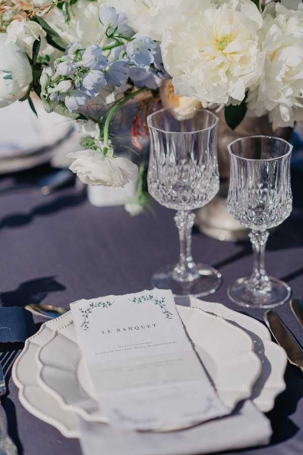 Crystal goblets and cream and blue wedding stationery menu that reads "Le Banquet"