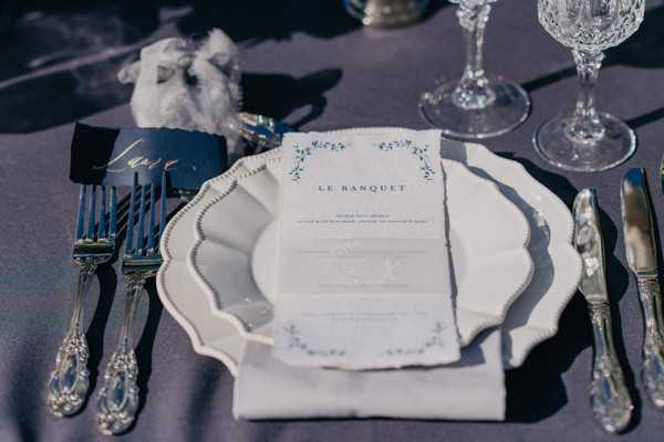 Wedding menu on white plate with silver cutlery and blue and gold nameplace holder