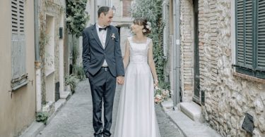 Bride and Groom stand in street of medieval town with stone buildings