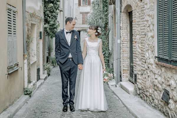 Bride and Groom stand in street of medieval town with stone buildings