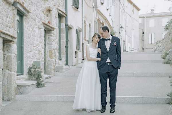 bride and groom stand in alleyway with stone buildings and green doors and shutters