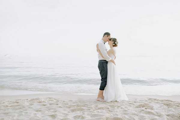 bride and groom barefoot in the sand embracing in front of ocean