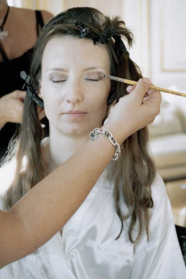 bride with eyes closed has hair and makeup applied