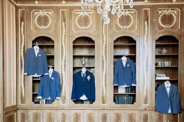 groom and groomsmen's blue suit jackets hand from wooden bookshelves 