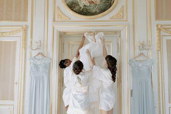 bride and bridesmaids take wedding gown down from hanger in door way