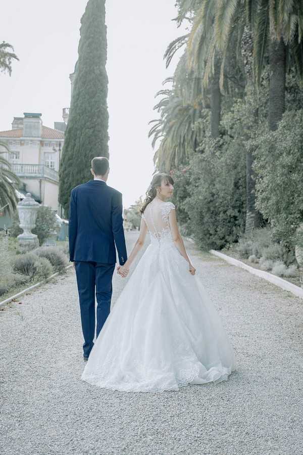 bride and groom walking away from camera along pebble path in garden of chateau