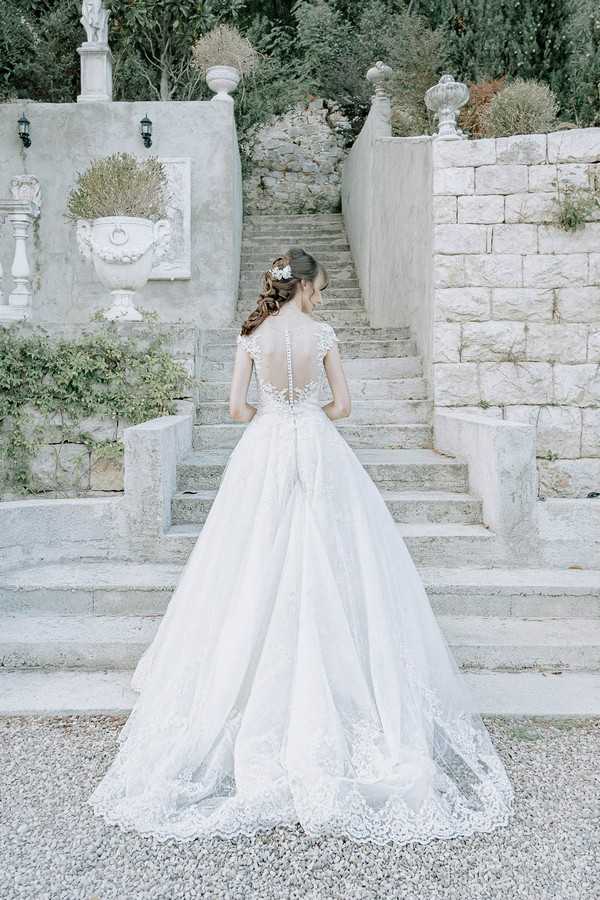 bride shows the back of her dress to camera it is made of white lace and has buttons up to the nape of her neck