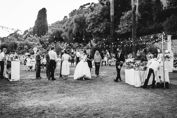 black and white image of wedding party on grass under festoon lighting for the after party