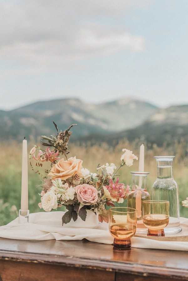simple couples wedding table arrangement on dark wood table in a field with mountain views