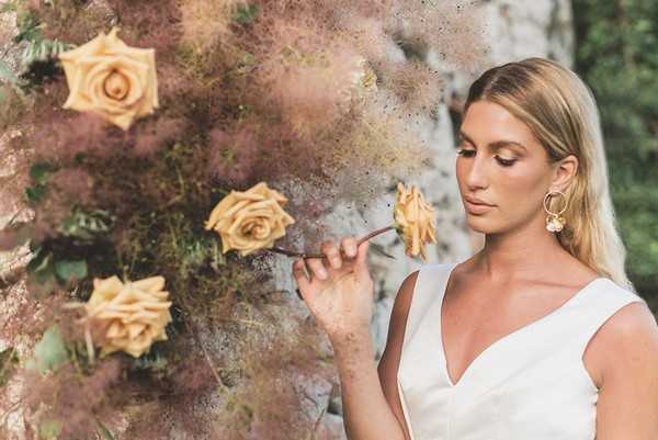 bride leans into to smell yellow roses and wears gold flower hoop earrings