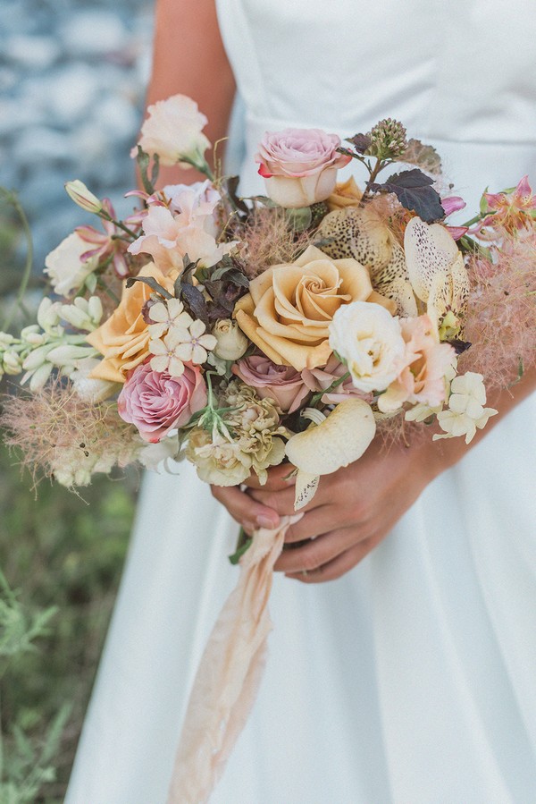 bridal bouquet in the hands of the bride with orchids, pink roses and cream lizzies