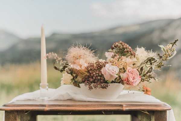 table with white candle and neutral toned floral arrangement in a field with mountain views