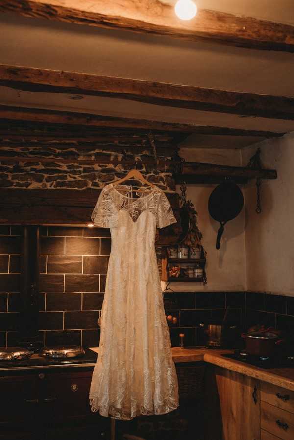 lace wedding dress hanging from old wooden beams inside farm house