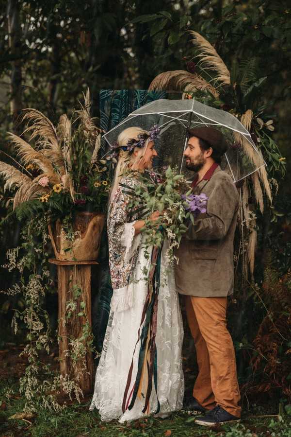 bride and groom surrounded by pampas grass under umbrella in the rain