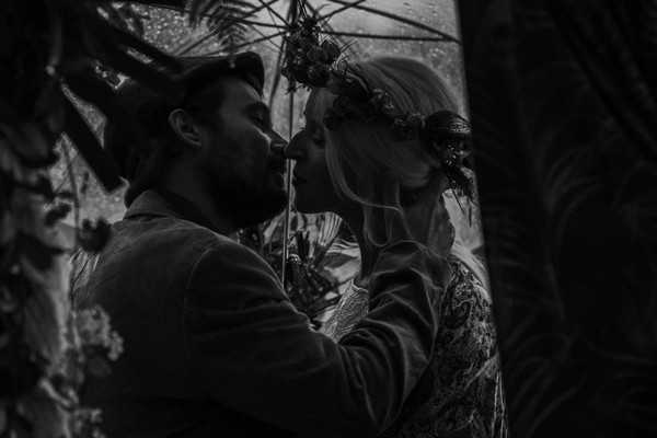 black and white image of bride and groom kissing under umbrella in rain