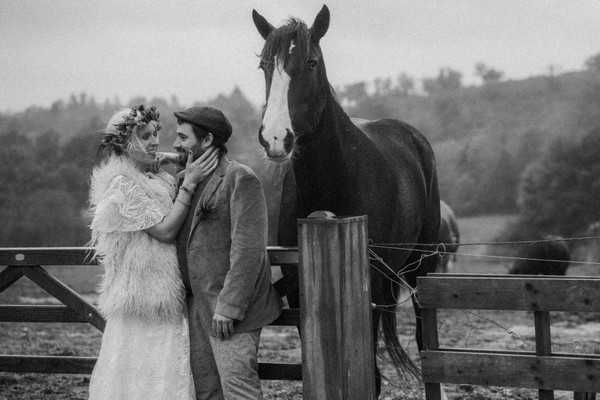 bride and groom stand next to shire horse in field