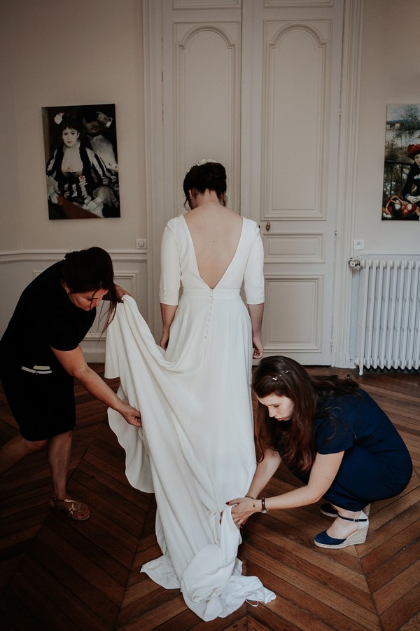 2 womens help bride put white low back wedding dress on